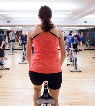 Group training instructor cycling on her bike in front of the class as they follow along on their stationary bikes.